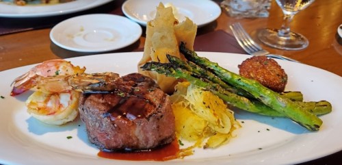 A gourmet plate featuring grilled shrimp, filet mignon, asparagus, and a crispy garnish, served with spaghetti squash.