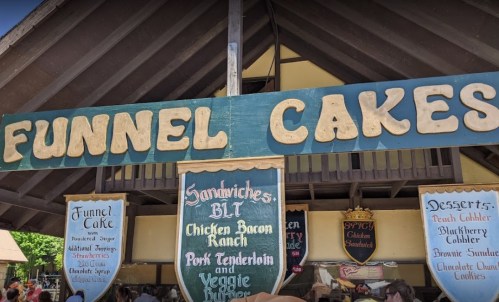 Sign for a food stand featuring funnel cakes, sandwiches, and desserts, with menu items listed below.
