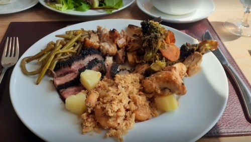 A plate of food featuring grilled meats, rice with vegetables, green beans, and roasted mixed vegetables.
