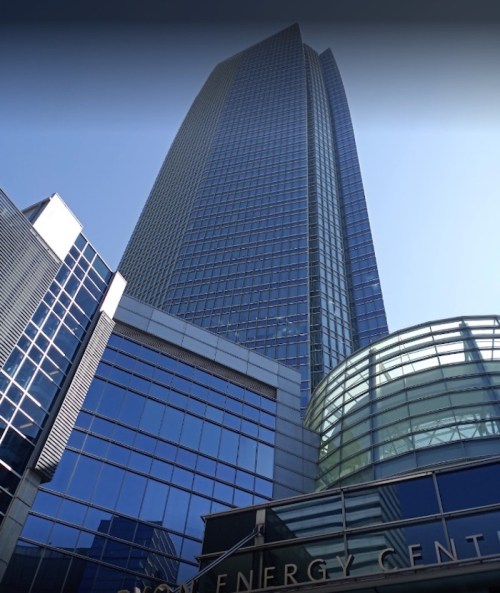 A tall modern skyscraper with glass facades, reflecting the blue sky, and a curved glass entrance at the base.