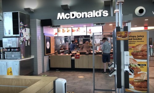 A McDonald's restaurant interior with customers ordering at the counter and a menu display on the side.