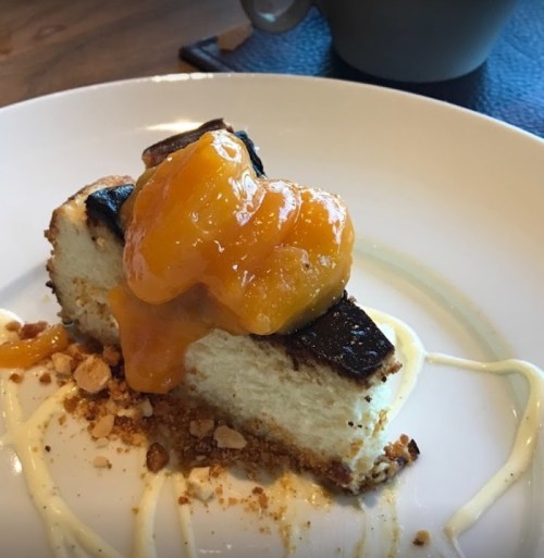 A slice of cheesecake topped with orange sauce and crushed nuts, served on a white plate.