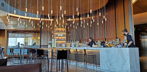 A modern bar with pendant lights, a marble counter, and two bartenders preparing drinks in a stylish interior.
