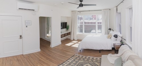 Bright, modern room with a bed, sofa, and TV, featuring large windows and wooden flooring.