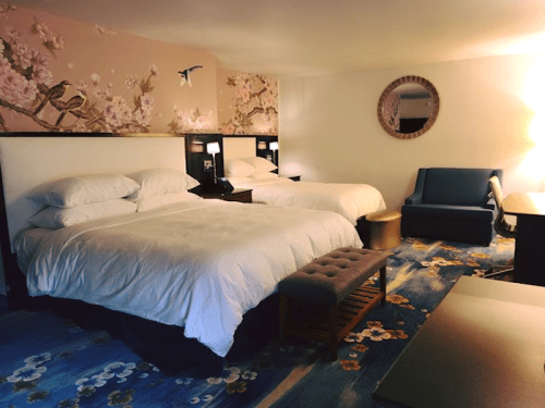 A cozy hotel room with two beds, a blue sofa, and floral decor on the walls and carpet.