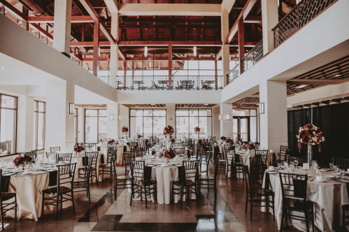 Elegant dining room set for an event, featuring round tables with floral centerpieces and a spacious, airy design.