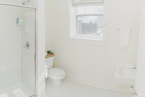 Bright, modern bathroom featuring a glass shower, toilet, sink, and large window with natural light.