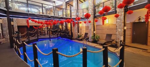 Indoor pool area with blue water, surrounded by stone walls and decorated with red lanterns and rope accents.