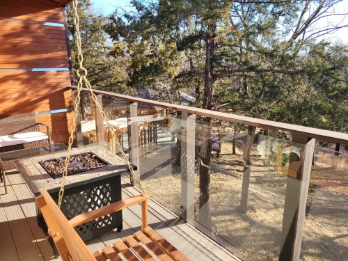 A wooden balcony with a swing chair and a fire pit, surrounded by trees and outdoor seating.