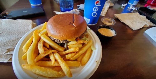 A plate with a burger and fries, alongside a cup of Pepsi and some condiments on a table.