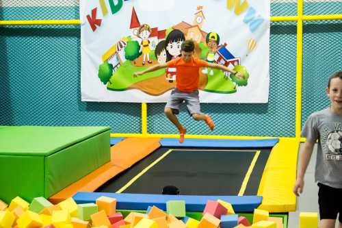 A child jumps on a trampoline surrounded by colorful foam blocks, with a playful backdrop featuring cartoon characters.