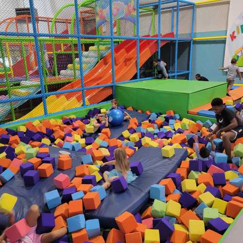 A colorful indoor play area filled with children playing in a foam pit surrounded by slides and climbing structures.