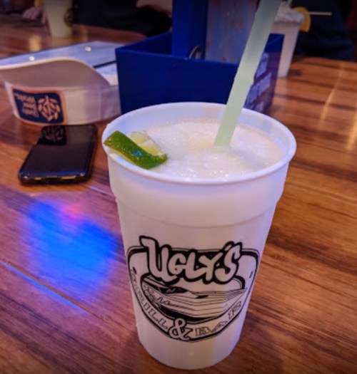 A frosty drink in a branded cup with a lime wedge and a straw, set on a wooden table.