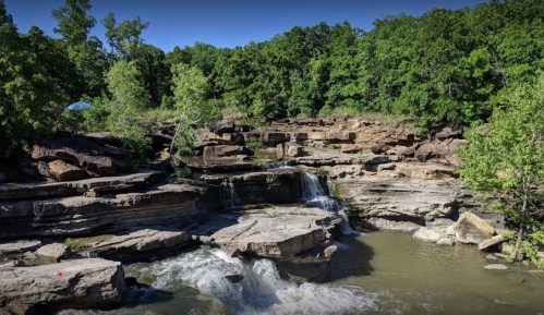 A serene landscape featuring a waterfall cascading over rocky terrain, surrounded by lush green trees.