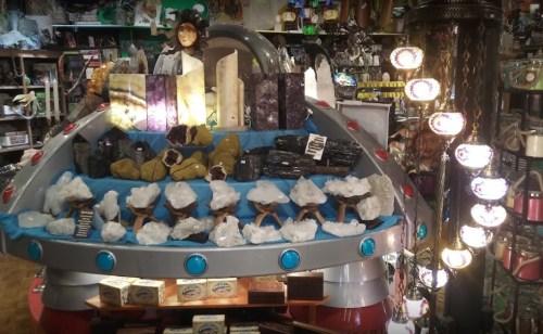 A display of crystals and stones on a UFO-shaped stand in a colorful shop filled with various mystical items.