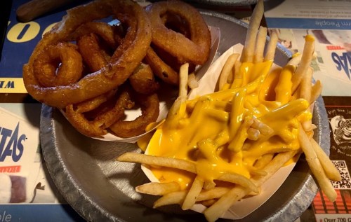A plate with crispy onion rings and cheese-covered French fries on a colorful table.