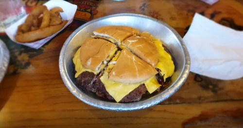 A cheeseburger cut in half, served in a metal dish, with melted cheese and a side of fries on a wooden table.