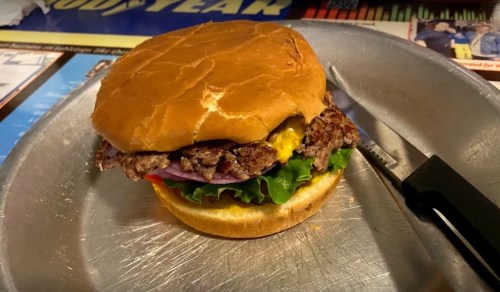 A juicy cheeseburger with lettuce, tomato, onion, and a toasted bun on a metal plate.