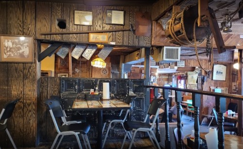 Cozy restaurant interior featuring wooden walls, a table with chairs, and rustic decor elements.