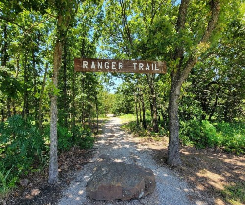 A wooden sign reading "Ranger Trail" marks a gravel path surrounded by lush greenery and trees.