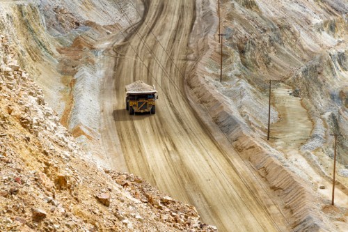 A large mining truck drives along a dirt road in a quarry, surrounded by steep, rocky terrain.