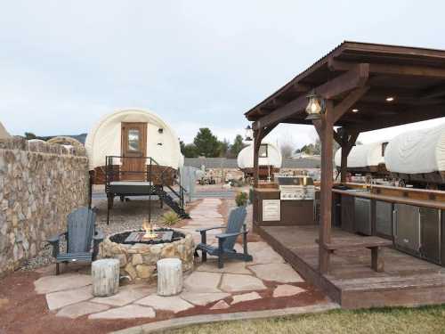 Cozy outdoor area with a fire pit, seating, and glamping tents in the background, surrounded by stone pathways.