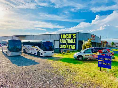 Two buses parked outside a large building with a sign for "Jack's Paintball Lasertag" and a dinosaur statue.