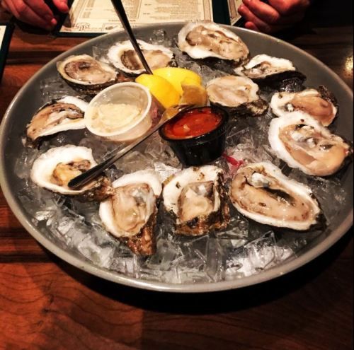 A platter of fresh oysters on ice, garnished with lemon wedges and dipping sauces.