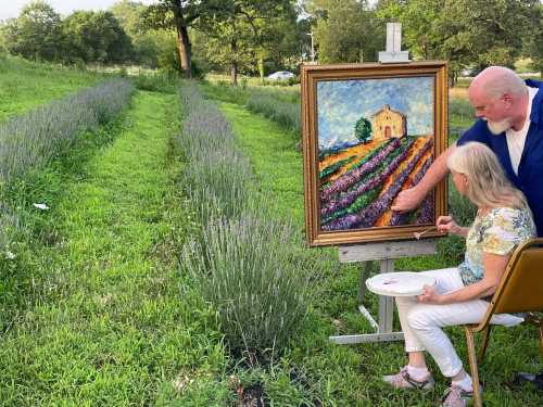 A man guides a woman painting a vibrant landscape in a lavender field, with rows of lavender in the background.