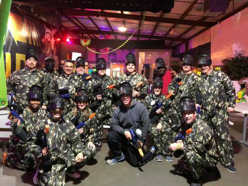 A group of people in camouflage outfits and masks, holding paintball guns, posing together in a recreational space.