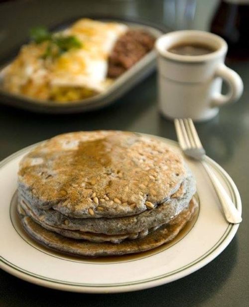 A stack of pancakes drizzled with syrup, served on a plate with a fork, and a cup of coffee in the background.