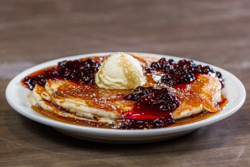A plate of pancakes topped with berry sauce, a scoop of ice cream, and a sprinkle of powdered sugar.