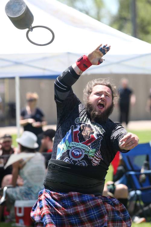 A man in a kilt throws a heavy weight during a competition, showing intense focus and effort.