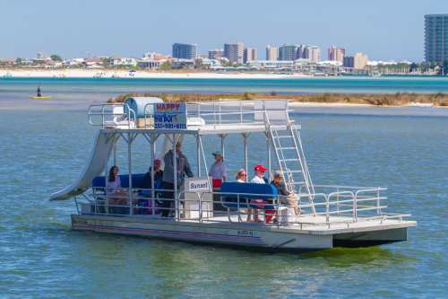 A tour boat with passengers enjoying a sunny day on the water, with a coastal city skyline in the background.
