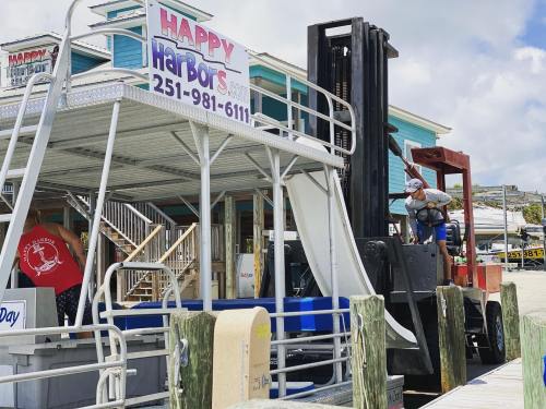 A dockside scene featuring a sign for Happy Harbors and a forklift unloading supplies. Bright, sunny day.