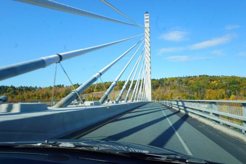 A view of a cable-stayed bridge with a tall tower, surrounded by colorful autumn foliage under a clear blue sky.