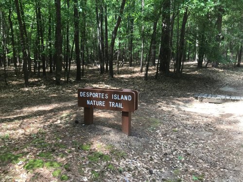 Sign for Desportes Island Nature Trail surrounded by trees and forest floor covered in leaves.