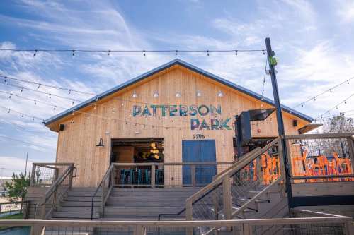 A wooden building with "Patterson Park" sign, outdoor seating, and string lights against a blue sky.