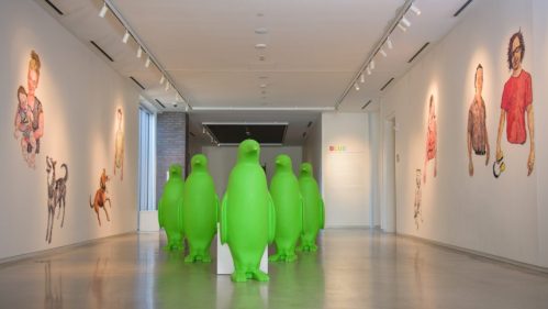 A gallery with large green penguin sculptures and colorful wall art featuring people and animals.