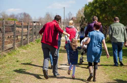 A group of people walking along a path in a rural area, enjoying a sunny day outdoors.