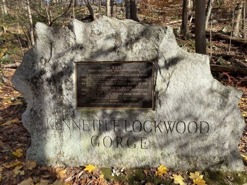 A large stone monument with a plaque honoring Kenneth E. Lockwood, surrounded by autumn foliage in a wooded area.