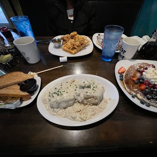 A table with plates of biscuits and gravy, waffles, pancakes topped with berries, and drinks.