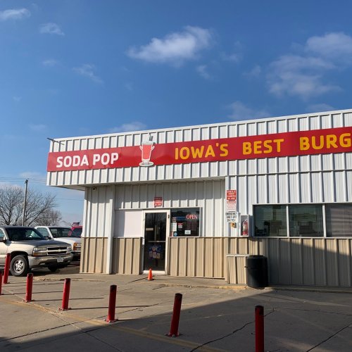 Exterior of a building with a sign reading "Soda Pop" and "Iowa's Best Burgers," under a blue sky.