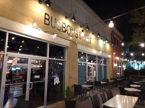 Exterior of Busboys and Poets restaurant at night, featuring string lights and outdoor seating.