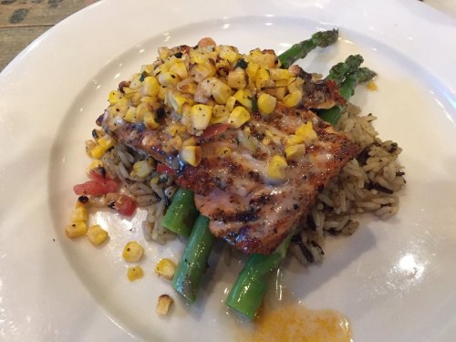 Grilled salmon topped with corn salsa, served on a bed of rice and asparagus, garnished with diced tomatoes.