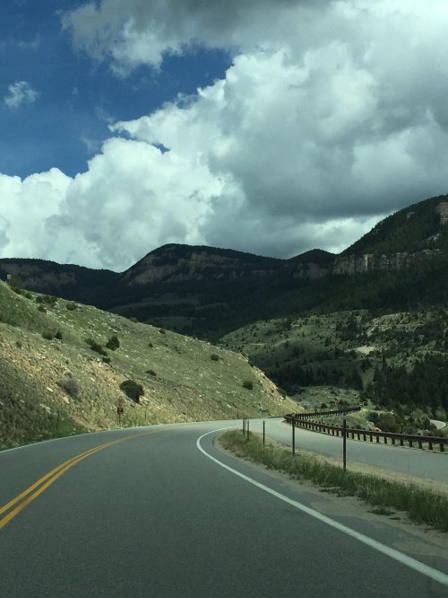 Winding road through green hills and mountains under a cloudy sky.