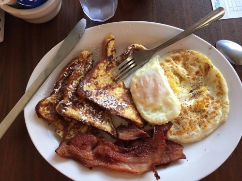 A plate of breakfast featuring French toast, a fried egg, and crispy bacon.
