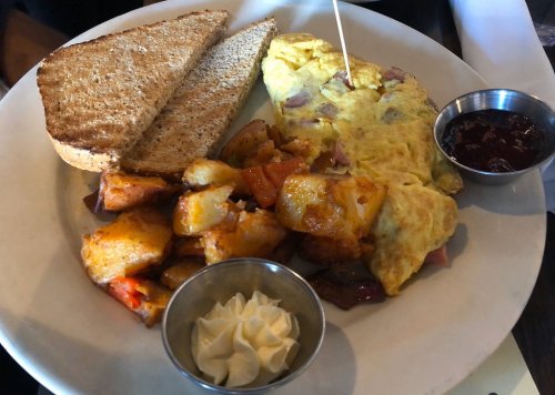 A plate with a fluffy omelette, toast, seasoned potatoes, and small bowls of jam and cream.