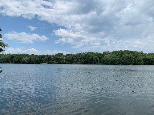 A serene lake surrounded by lush green trees under a partly cloudy sky.