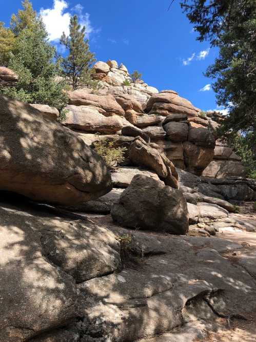 Rocky landscape with large boulders and trees under a blue sky with scattered clouds.